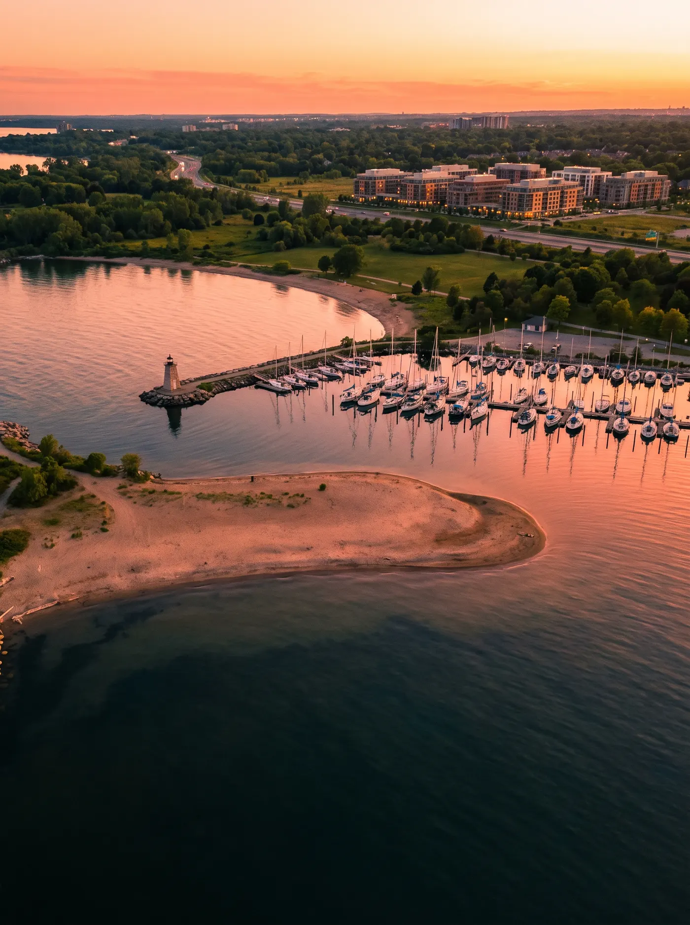 Golden-hour aerial view of a marina, a lighthouse and a sandy spit on the Lake Ontario shore